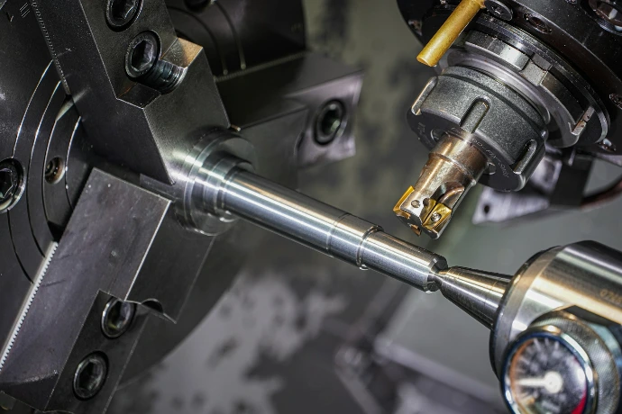 A metal rod held in a lathe chuck being machined by a cutting tool